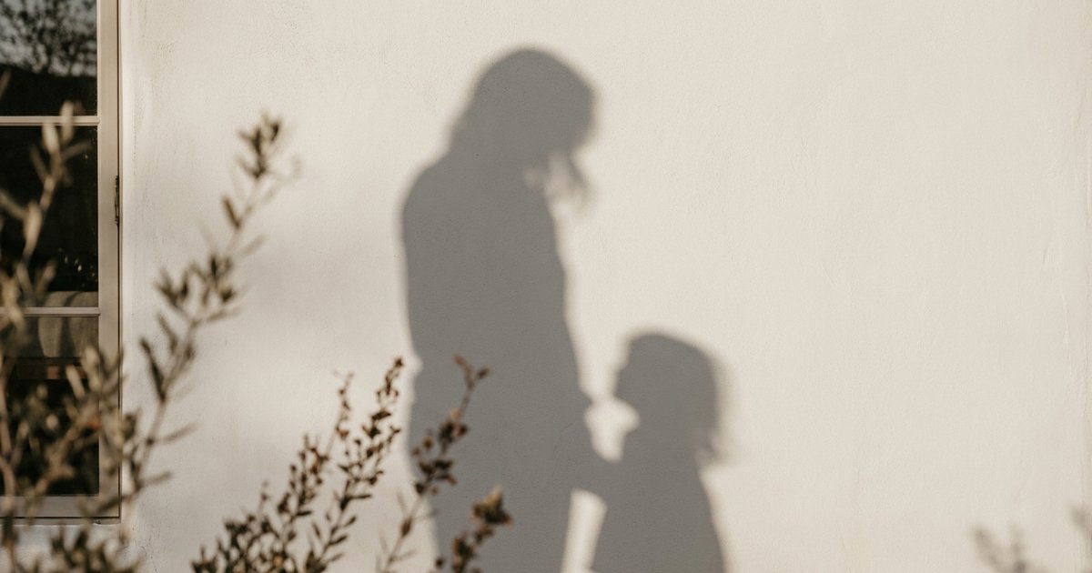 Le ombre di un adulto e di un bambino proiettate sullo stesso muro chiaro, quasi sovrapposte