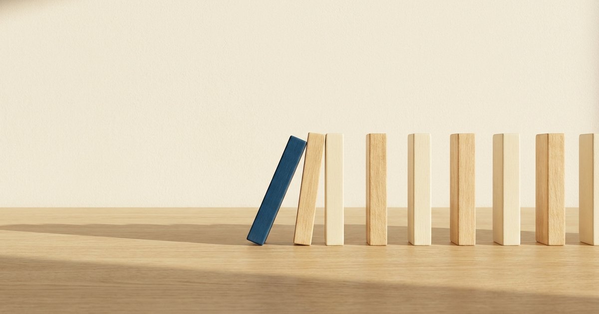 Impulsività negli adulti: una fila di tessere di legno chiaro su un tavolo, con una tessera blu inclinata che sta per cadere sulle altre, in una luce calda