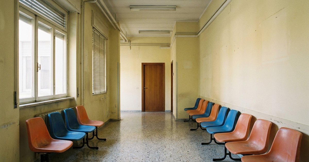 Sala d'attesa di un poliambulatorio pubblico italiano con sedie vuote allineate lungo un corridoio