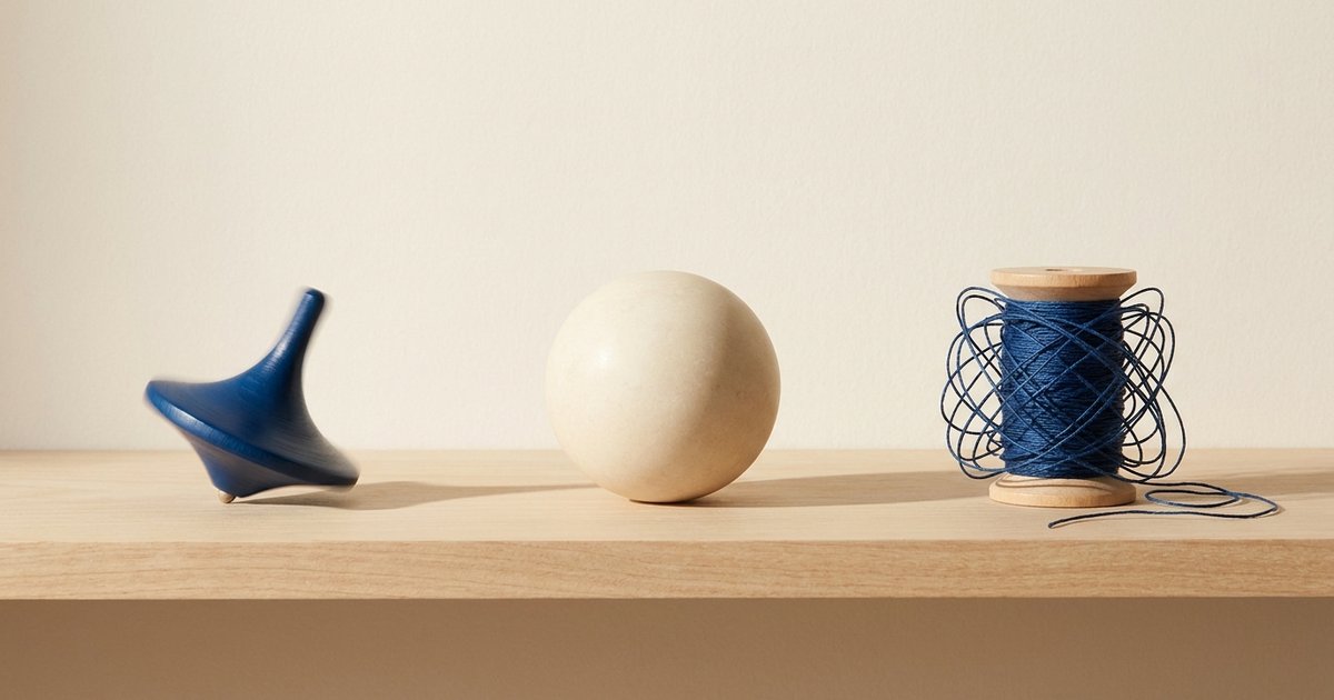 Tipi di ADHD negli adulti: una trottola blu in movimento, una sfera color crema ferma e un rocchetto con filo blu arruffato su una mensola di legno chiaro